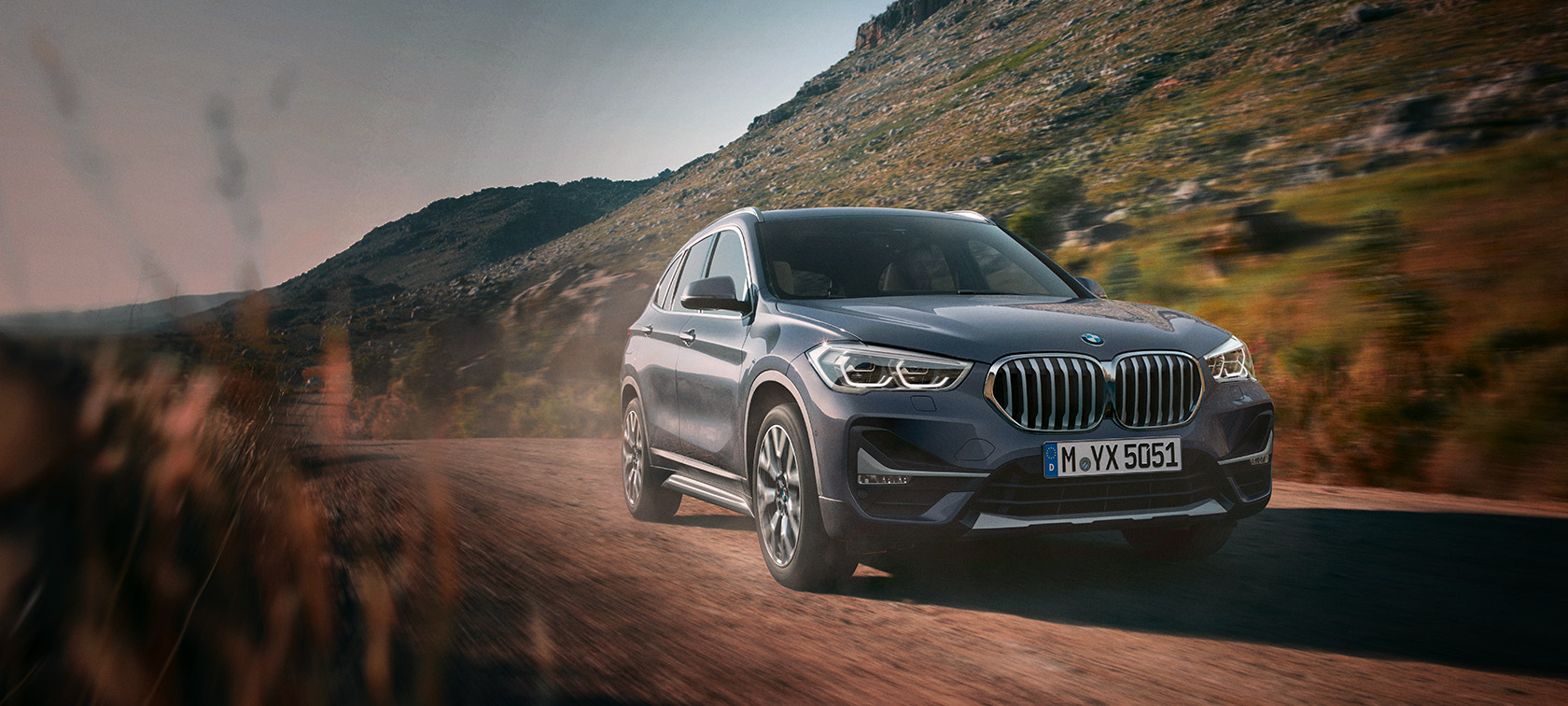 BMW X1 F48 LCI Storm Bay vue de trois quarts avant devant un paysage de montagnes