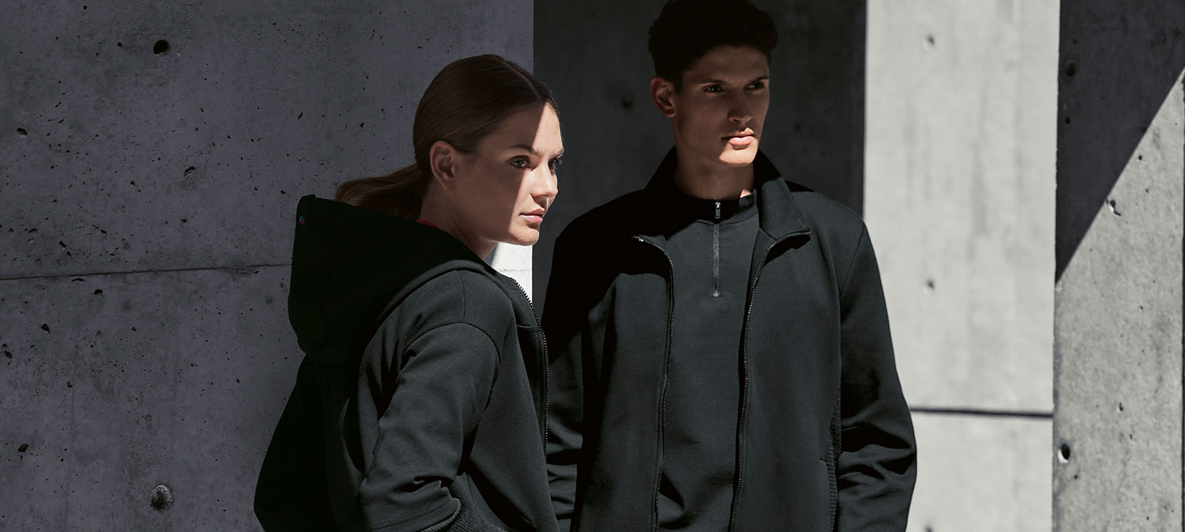 Veste sweat BMW M pour femme et veste sweat BMW M pour homme. Un couple est dans l'ombre. Une femme présente la veste sweat BMW pour femme et un homme porte la veste sweat BMW pour homme.
