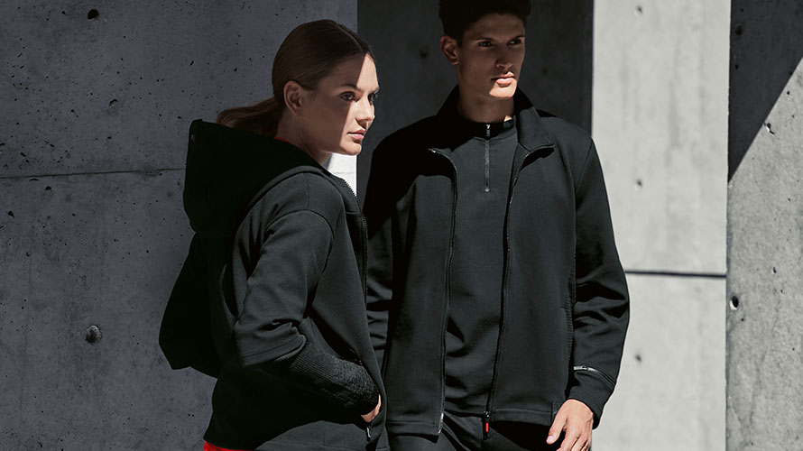 Un couple est dans l'ombre. Une femme présente la veste sweat BMW pour femme et un homme porte la veste sweat BMW pour homme.