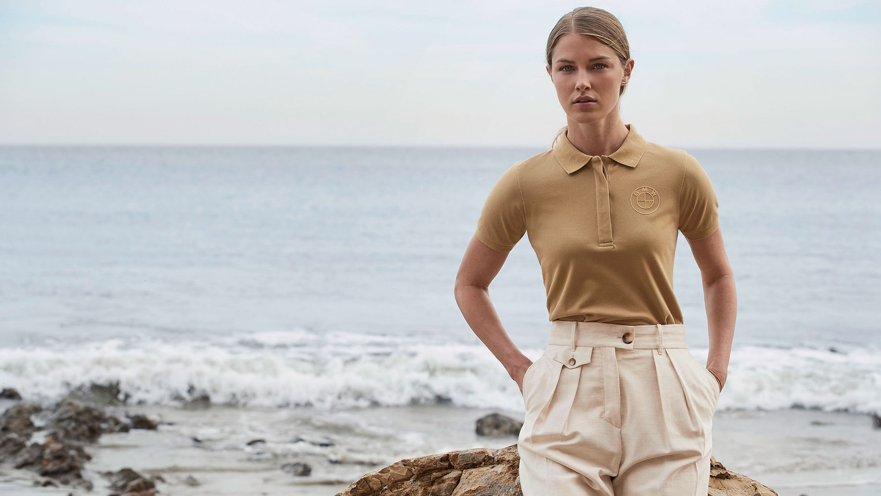 Une jeune femme porte le polo BMW avec logo pour femme devant un décor de plage. Une jeune femme porte le polo BMW avec logo pour femme devant un décor de plage.