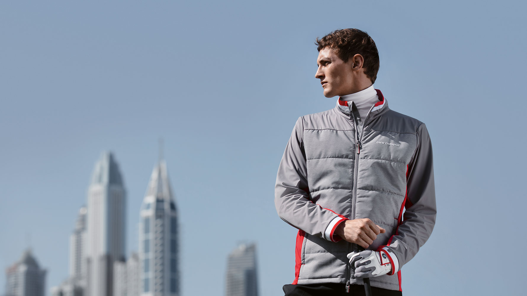 Un homme présente les articles de la collection BMW Golfsport devant la skyline d’une grande ville. Un homme présente les articles de la collection BMW Golfsport devant la skyline d’une grande ville.