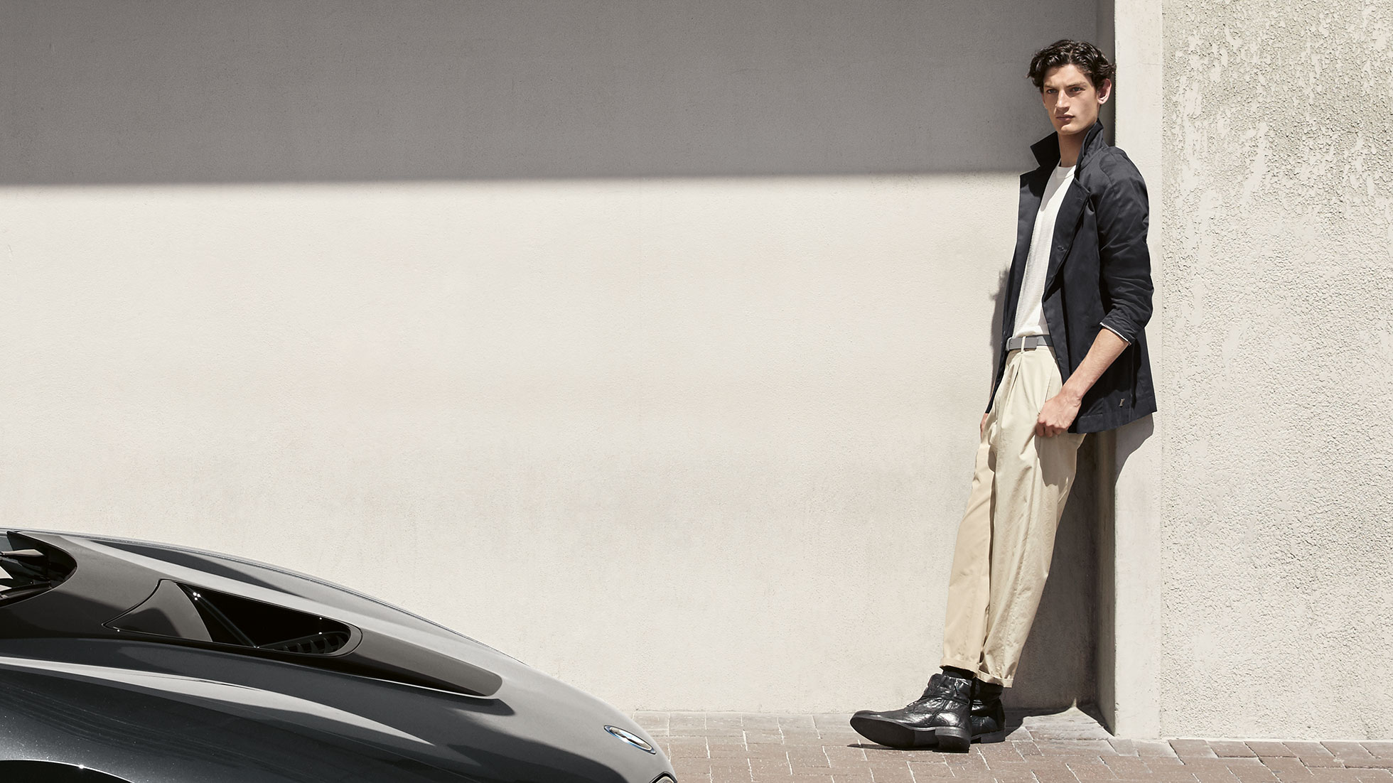 Collection BMW i. Sur la photo, un homme est appuyé contre un mur et porte le blouson BMW i de la collection BMW i.