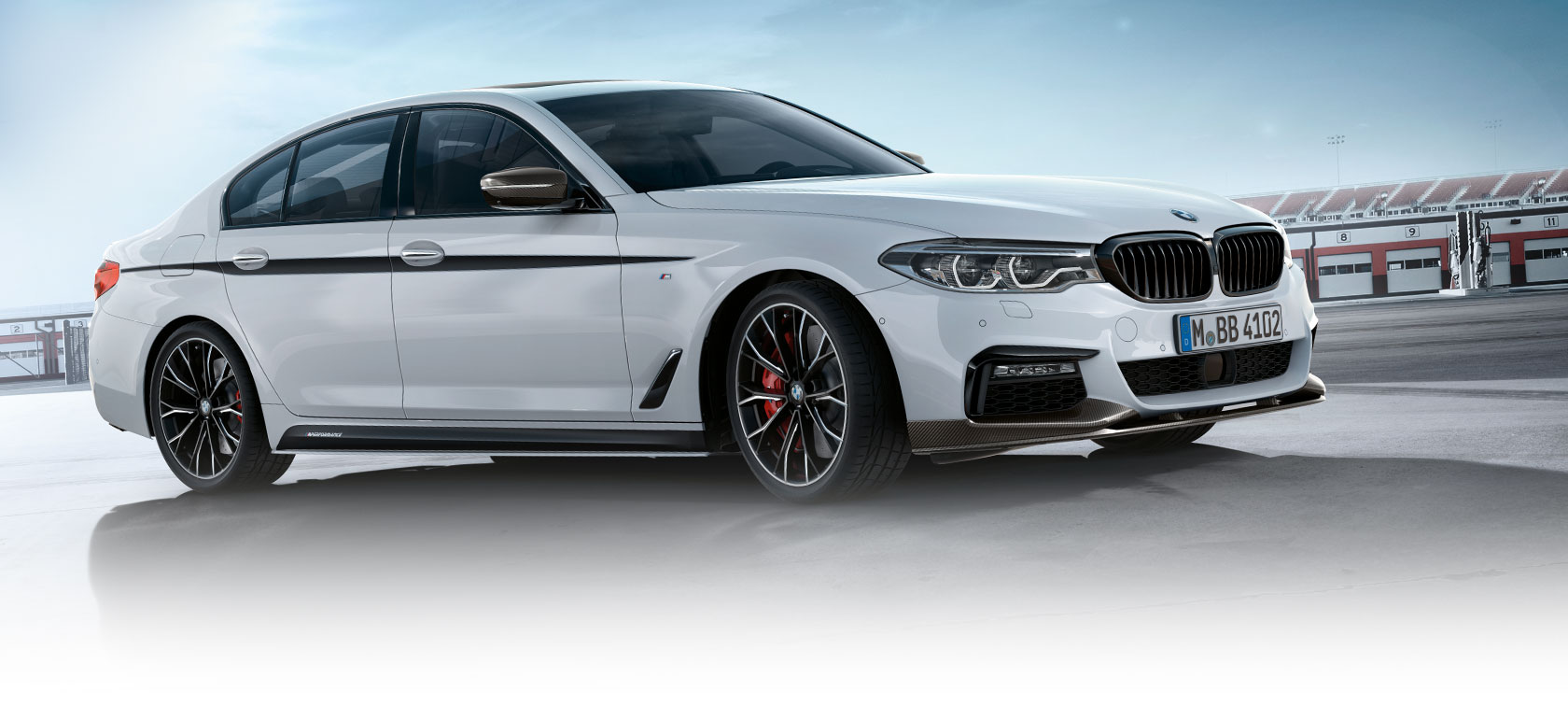 BMW 3 Series Sedan avec accessoires M Performance Parts. Vue latérale du modèle BMW 3 Series Sedan sur un parking sous un ciel bleu.